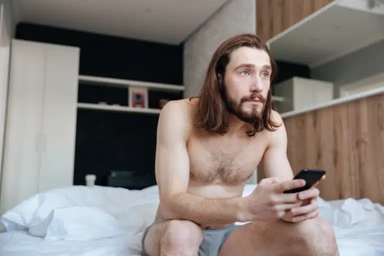 homme assis sur son lit devant son téléphone